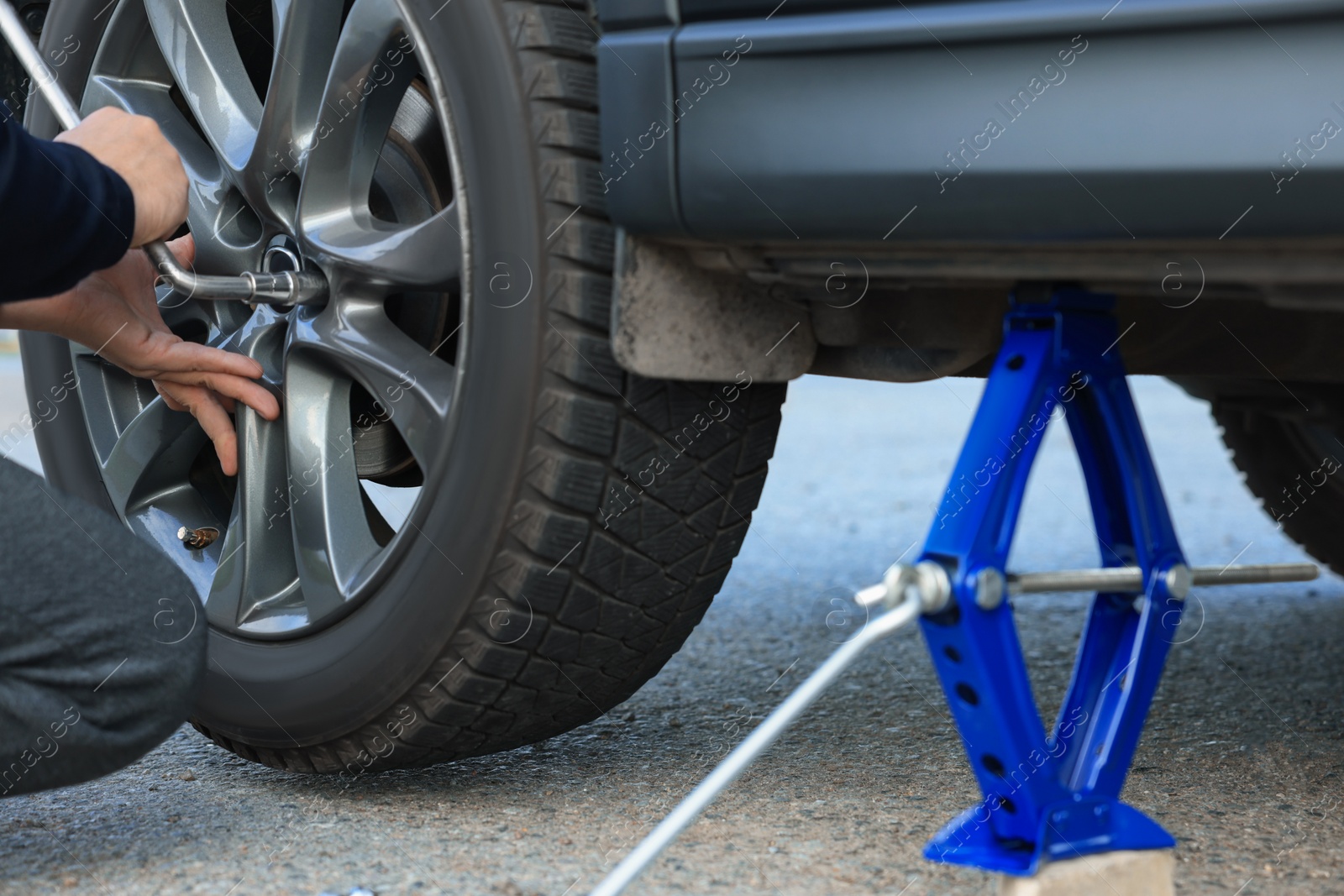 Photo of Man changing tire of car outdoors, closeup