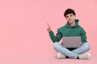 Photo of Portrait of student with laptop pointing on pink background. Space for text