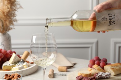 Woman pouring white wine from bottle into glass at table with snacks, closeup