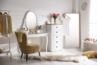 Stylish room interior with elegant dressing table, mirror and comfortable chair