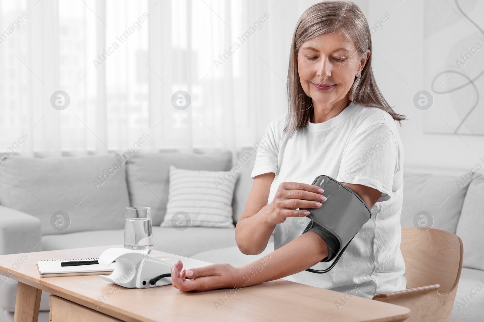 Photo of Woman measuring blood pressure at wooden table in room, space for text