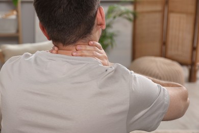 Man suffering from neck pain in living room, back view