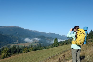 Photo of Tourist with hiking equipment looking through binoculars in mountains
