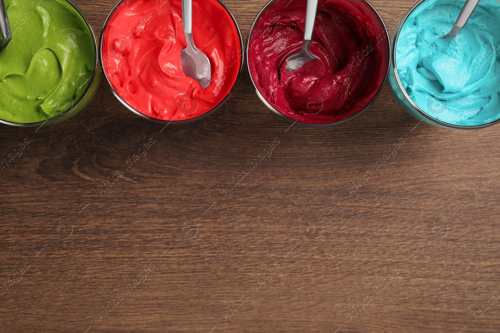 Photo of Glasses of different cream with food coloring on wooden table, flat lay. Space for text