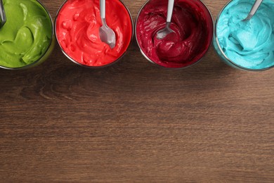 Photo of Glasses of different cream with food coloring on wooden table, flat lay. Space for text