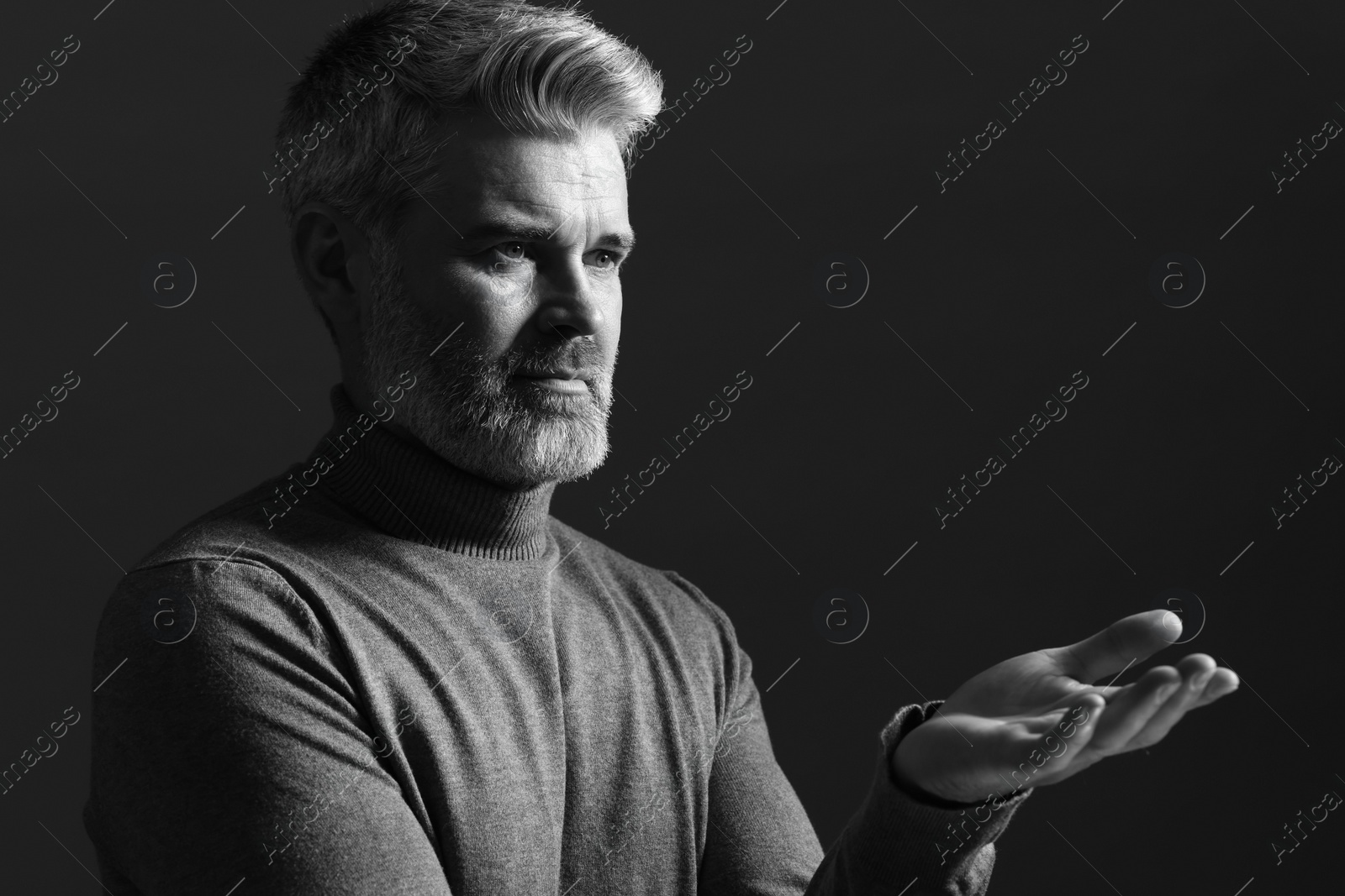 Photo of Portrait of handsome man gesturing on dark background. Black and white effect