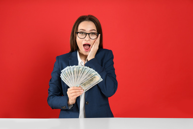 Photo of Emotional young woman with money at table on crimson background