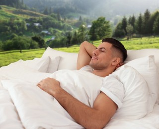 Image of Happy man sleeping in bed and beautiful view of mountain landscape on background. Sleep well - stay healthy