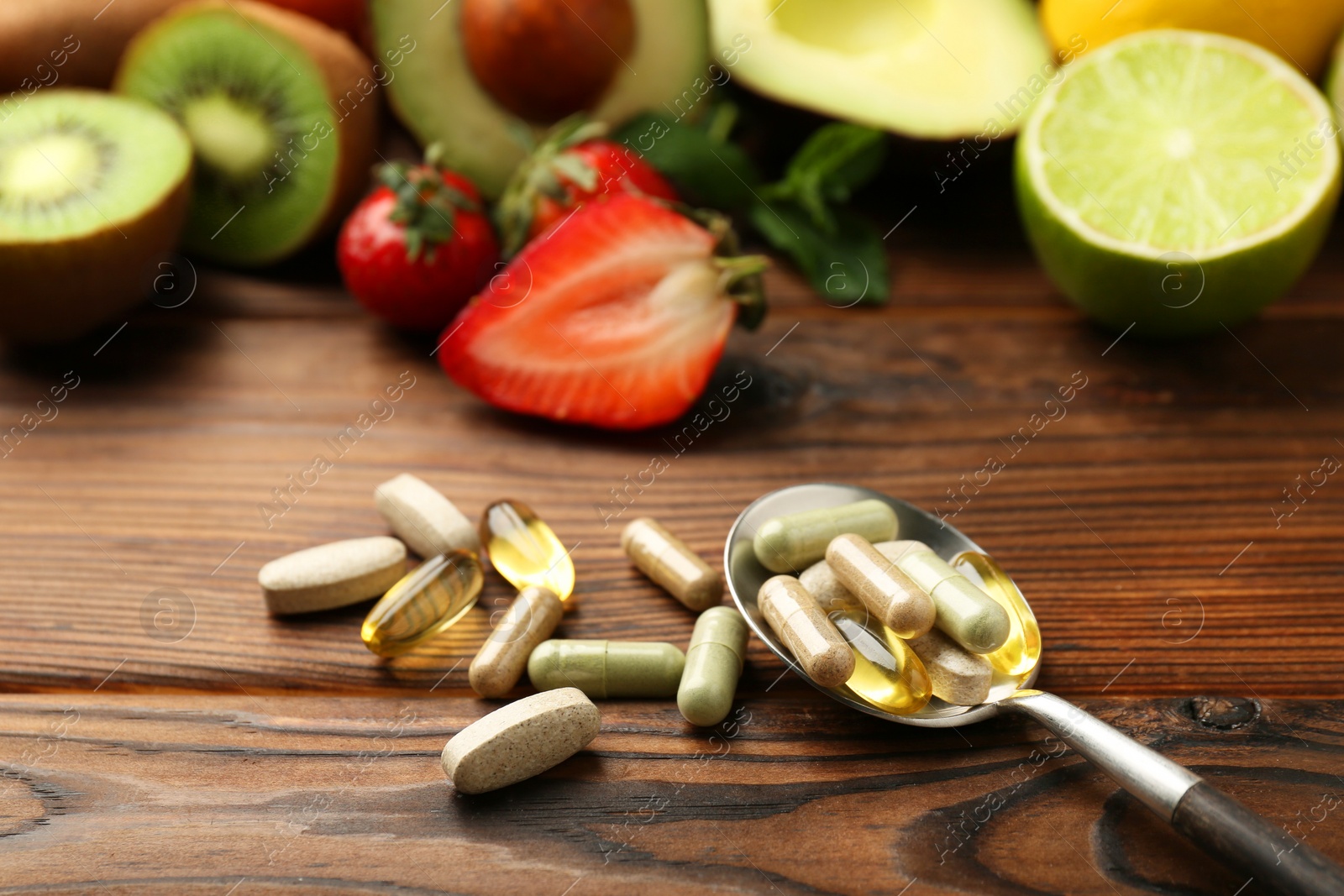 Photo of Different vitamin pills and fresh fruits on wooden table