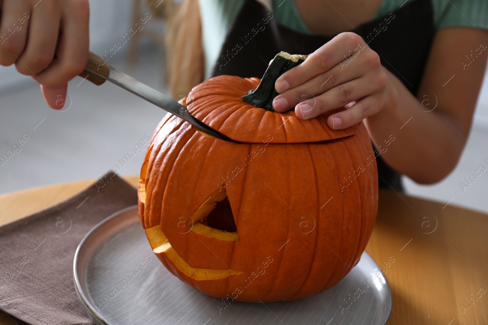 Photo of Woman making pumpkin jack o'lantern at wooden table, closeup. Halloween celebration