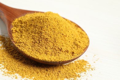 Curry powder in spoon on white wooden table, closeup