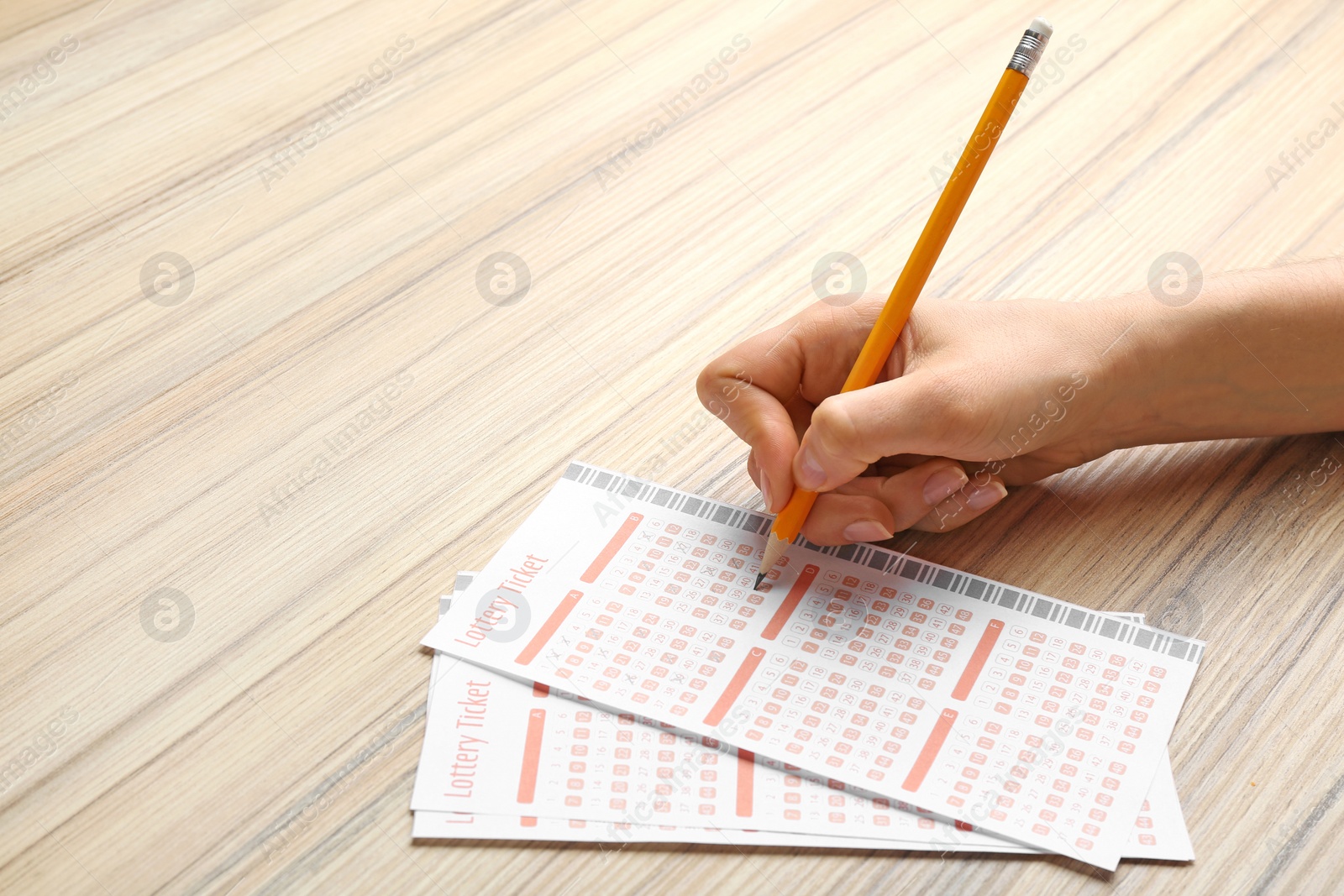 Photo of Woman filling out lottery tickets with pencil on wooden table, closeup. Space for text