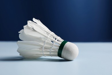 Feather badminton shuttlecock on light table against blue background, closeup. Space for text