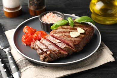 Photo of Delicious grilled beef steak served with spices and tomatoes on black table, closeup