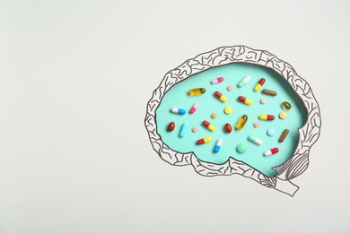 Pills on turquoise background, top view through paper with brain shaped hole and drawing. Space for text