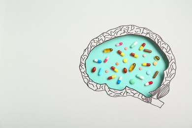 Photo of Pills on turquoise background, top view through paper with brain shaped hole and drawing. Space for text