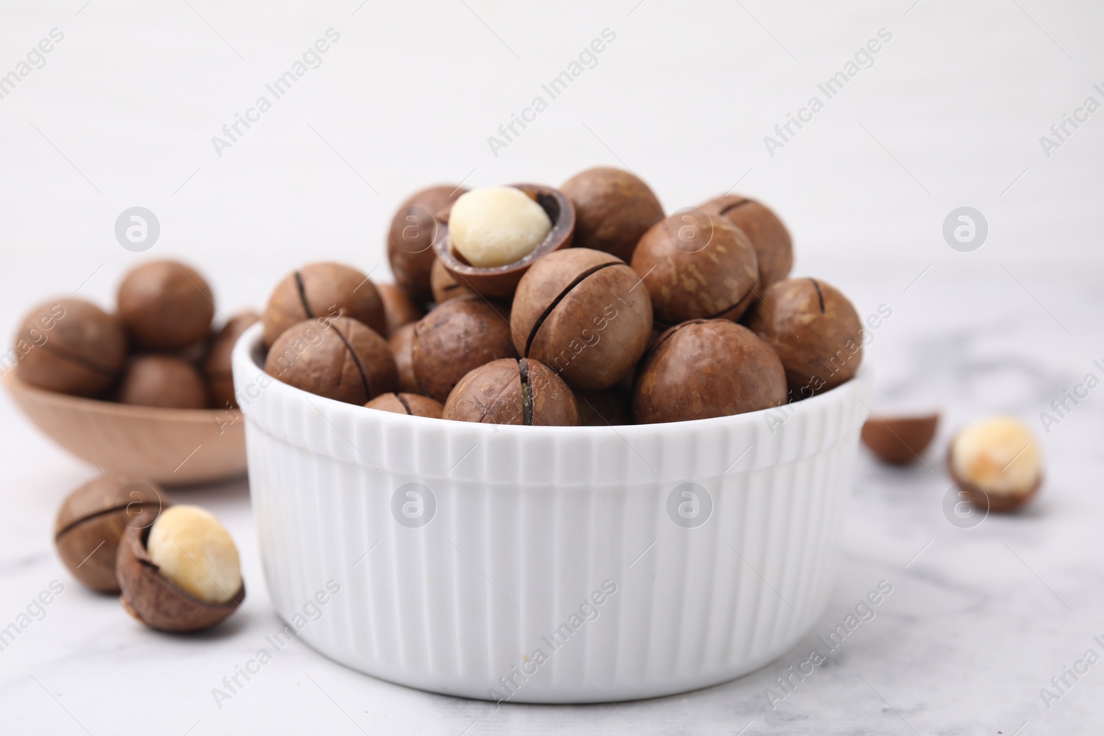 Photo of Tasty Macadamia nuts in bowl on white table, closeup