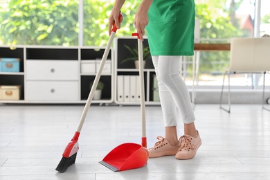 Young woman with broom and dustpan cleaning in office