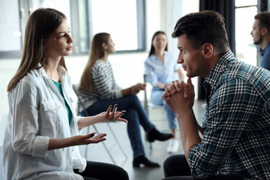 Photo of Psychotherapist working with patient in group therapy session indoors