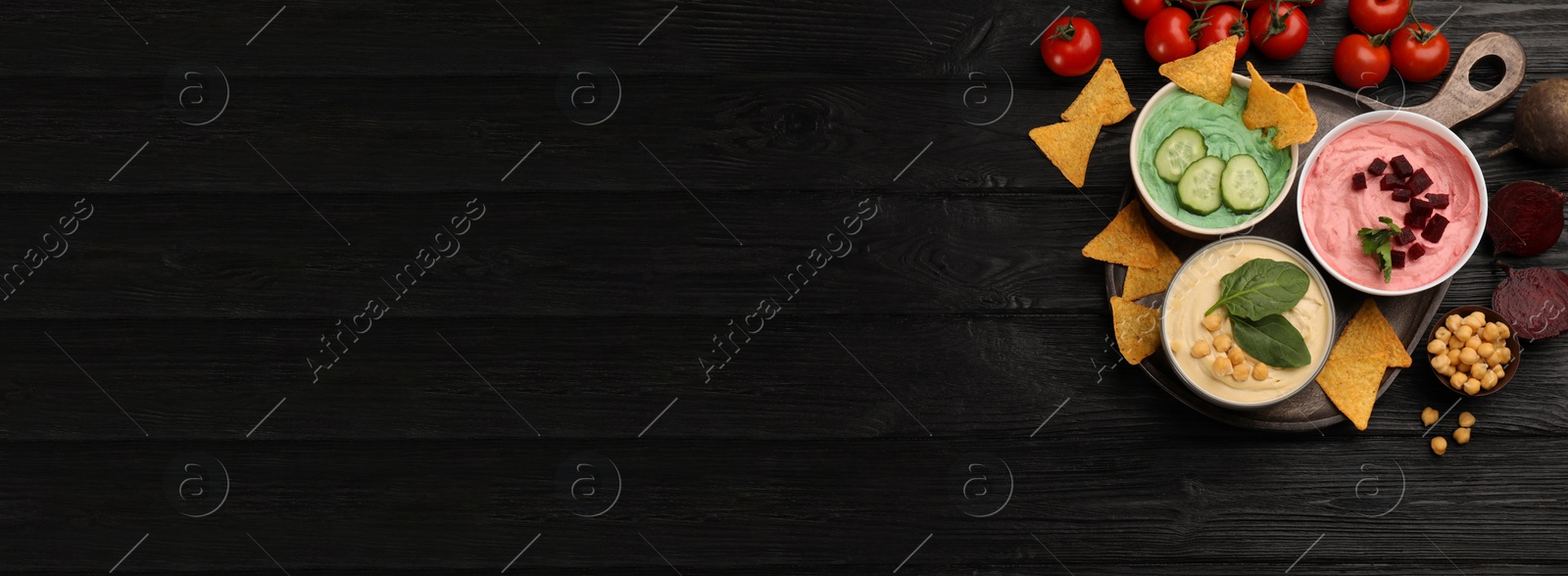 Image of Different delicious hummuses and tortilla chips on black wooden table, flat lay with space for text. Banner design