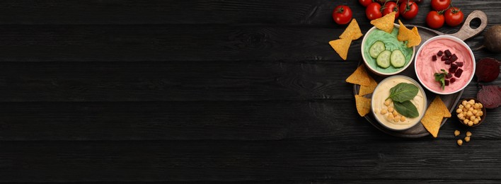 Image of Different delicious hummuses and tortilla chips on black wooden table, flat lay with space for text. Banner design