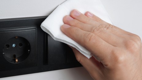 Photo of Man cleaning light switch with wet wipe indoors, closeup. Protective measures