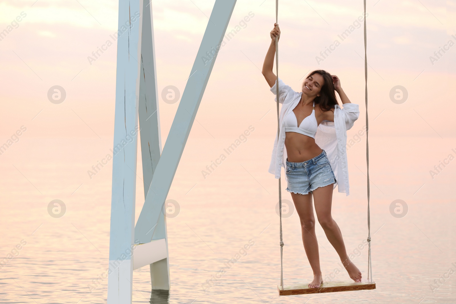 Photo of Young woman enjoying sunrise on swing over water