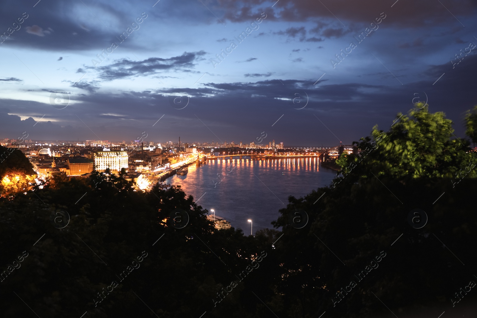 Photo of KYIV, UKRAINE - MAY 21, 2019: Beautiful view of night cityscape with illuminated buildings near river and bridge