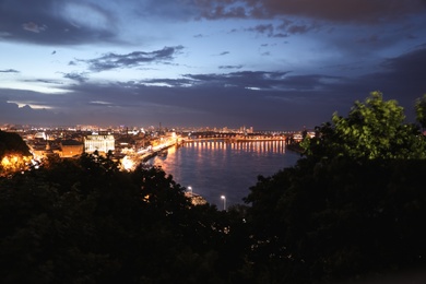 KYIV, UKRAINE - MAY 21, 2019: Beautiful view of night cityscape with illuminated buildings near river and bridge