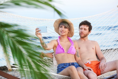 Young couple taking selfie in hammock on beach