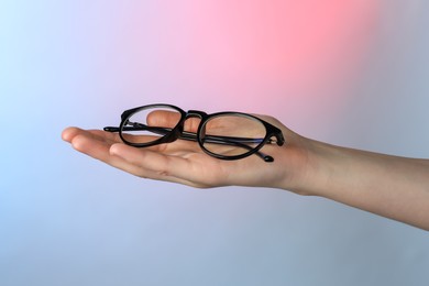 Woman holding glasses with black frame on color background, closeup