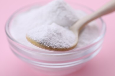 Bowl and spoon of sweet powdered fructose on pink background, closeup