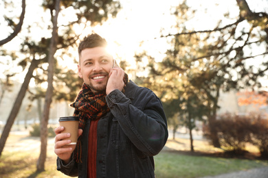 Photo of Man with cup of coffee talking on smartphone in morning outdoors