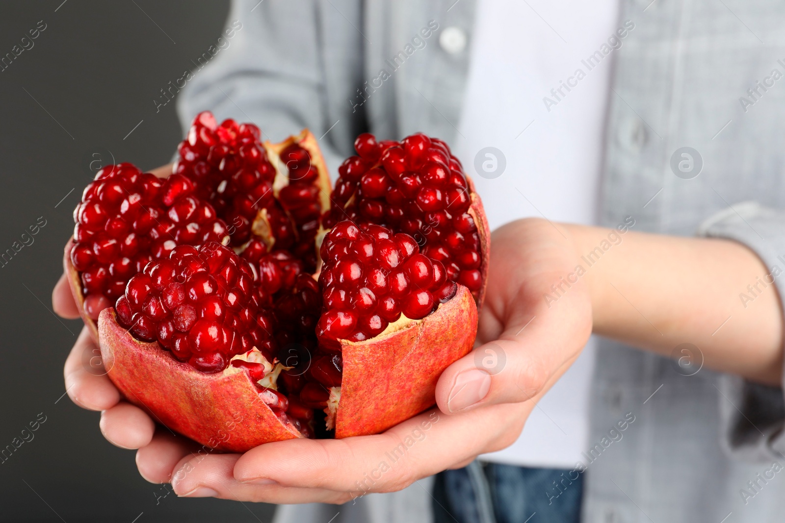 Photo of Woman holding fresh pomegranate on grey background, closeup