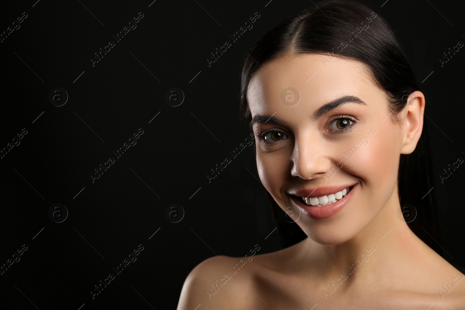 Photo of Portrait of happy young woman with beautiful black hair and charming smile on dark background, space for text