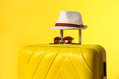 Photo of Stylish suitcase with hat and sunglasses on color background