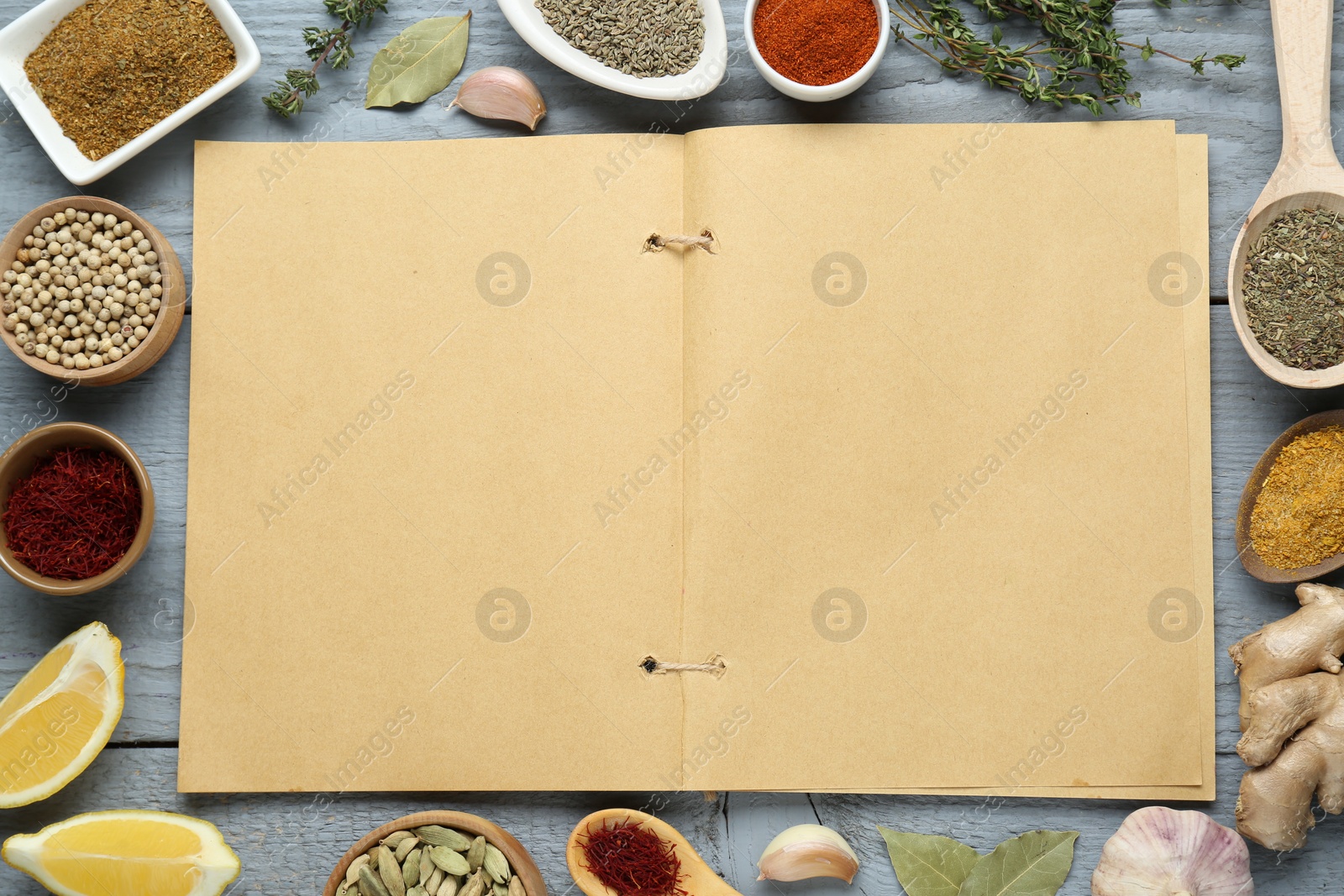 Photo of Blank recipe book surrounded by different ingredients on grey wooden table, flat lay. Space for text