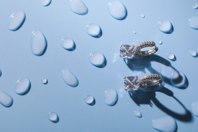 Photo of Luxury jewelry. Elegant earrings on light blue surface covered with water drops, flat lay and space for text