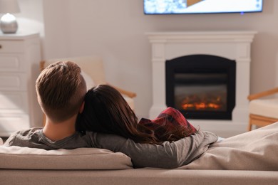 Photo of Lovely couple spending time together on sofa near fireplace at home, back view