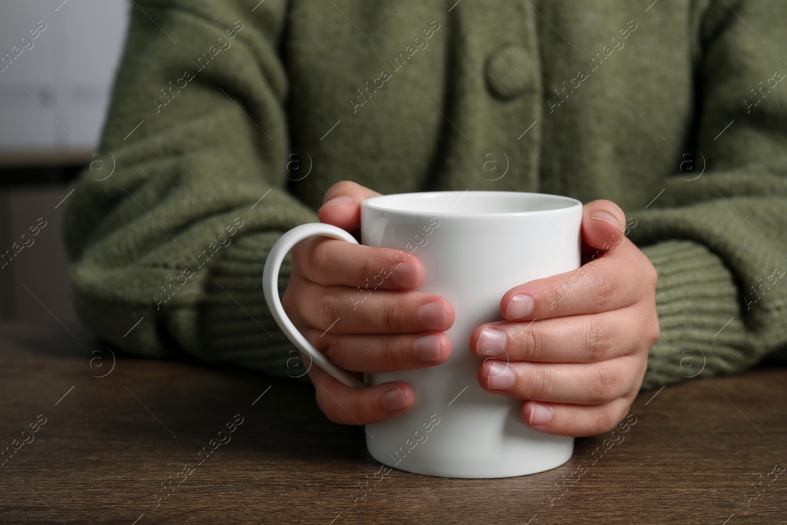 Photo of Woman holding white mug at wooden table, closeup