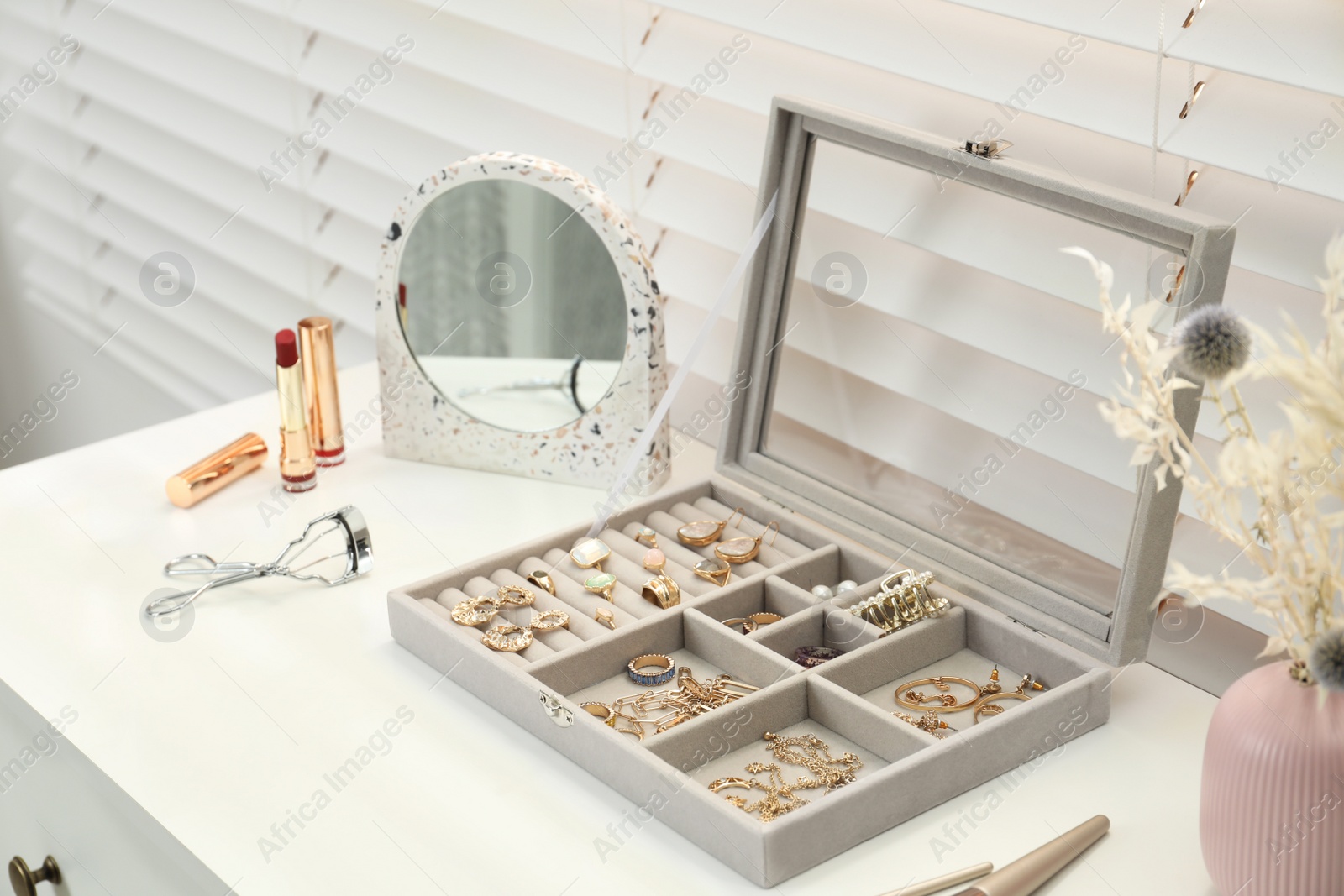 Photo of Elegant jewelry box with beautiful bijouterie and makeup products on dressing table indoors