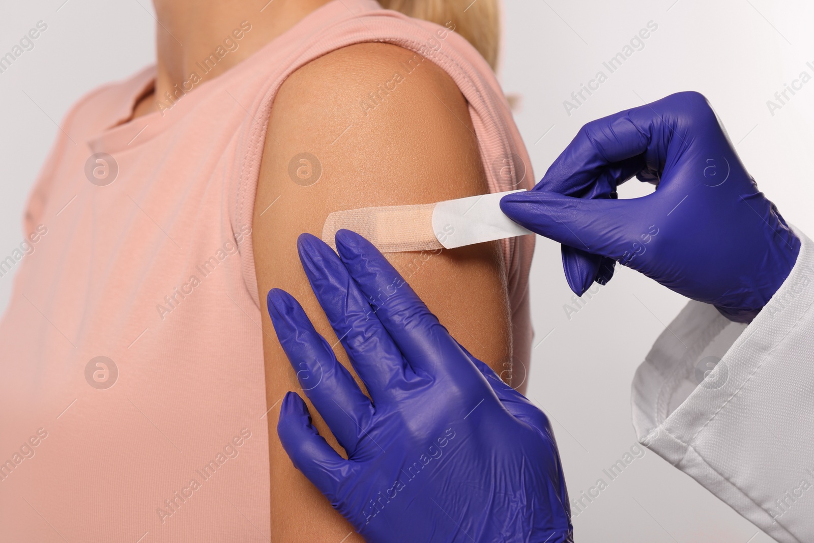 Photo of Nurse sticking adhesive bandage on woman's arm after vaccination on light background, closeup