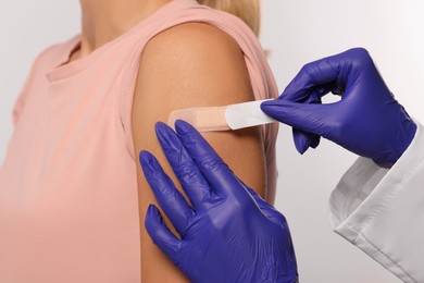 Photo of Nurse sticking adhesive bandage on woman's arm after vaccination on light background, closeup