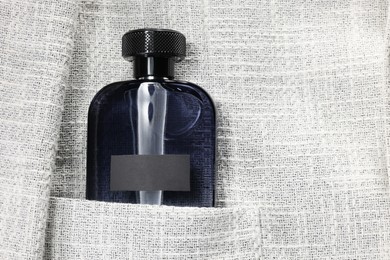 Photo of Luxury men's perfume in pocket of grey jacket, top view. Space for text