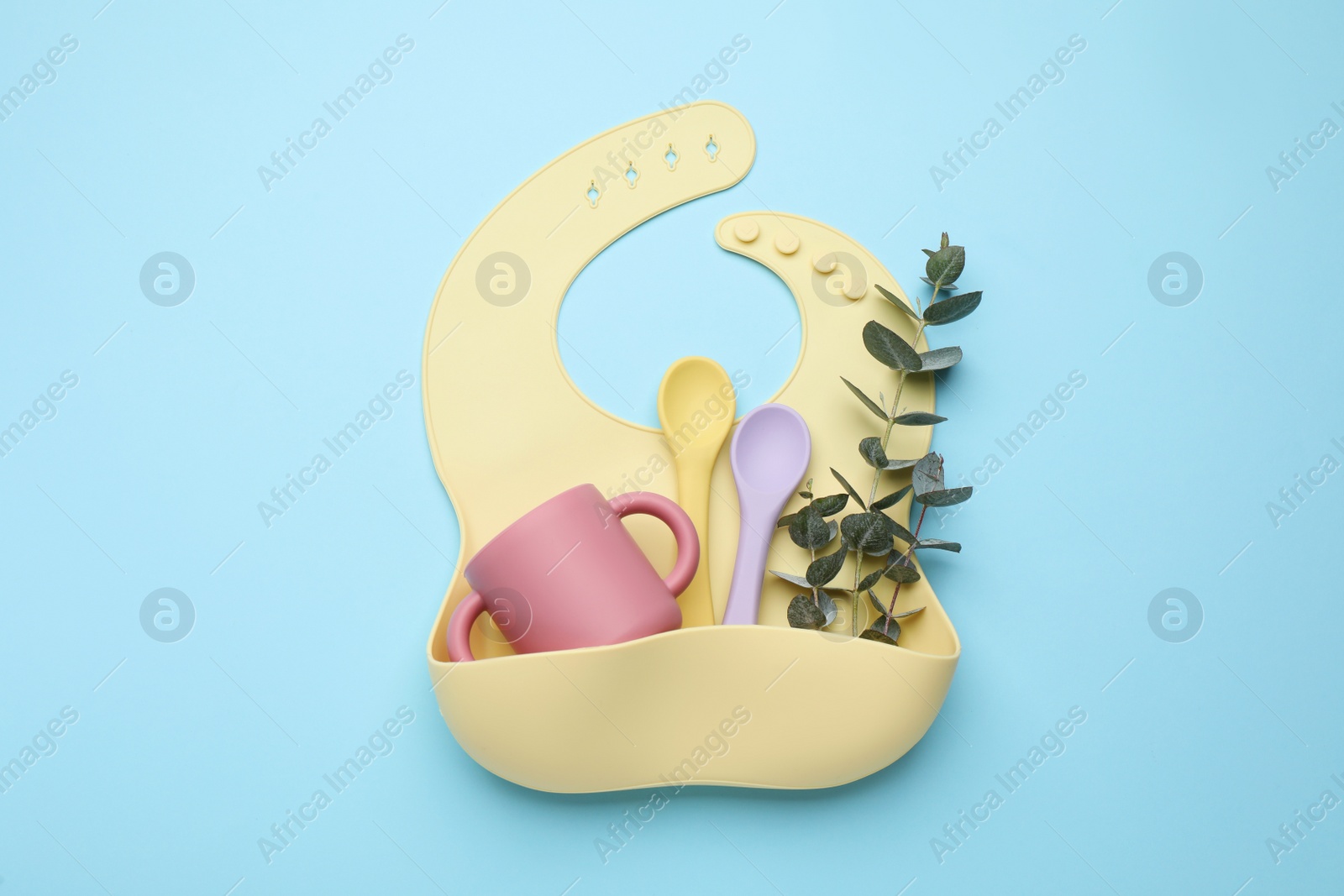 Photo of Baby feeding accessories and bib on light blue background, top view