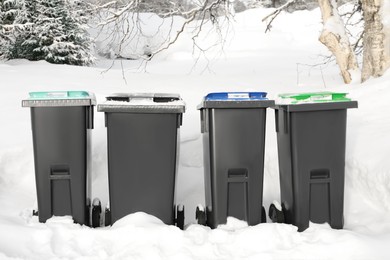 Photo of Many black recycling bins on snow outdoors. Winter season