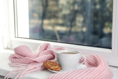 Photo of Cup of winter drink, cookie and knitted scarf on windowsill. Space for text