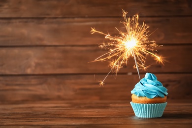 Delicious birthday cupcake with sparkler on table