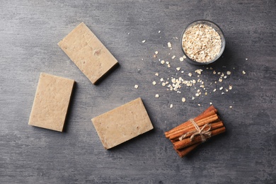 Photo of Handmade soap bars, oatmeal and cinnamon sticks on grey background, top view