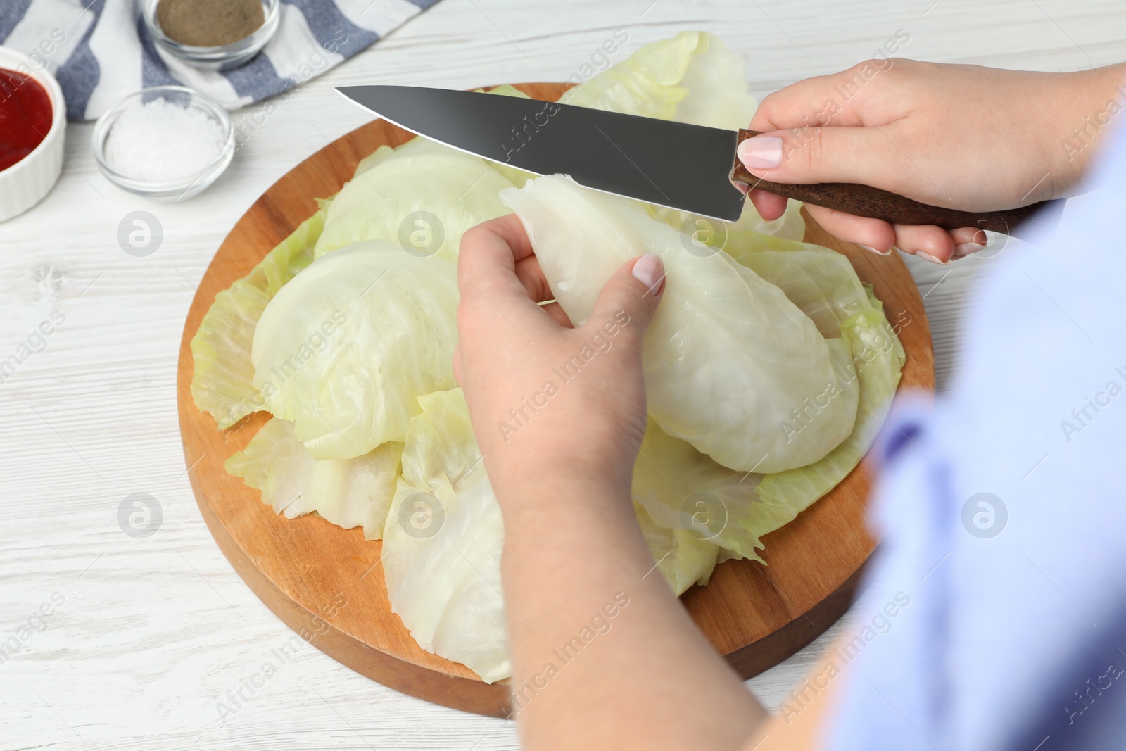 Photo of Woman preparing stuffed cabbage rolls at white wooden table, closeup